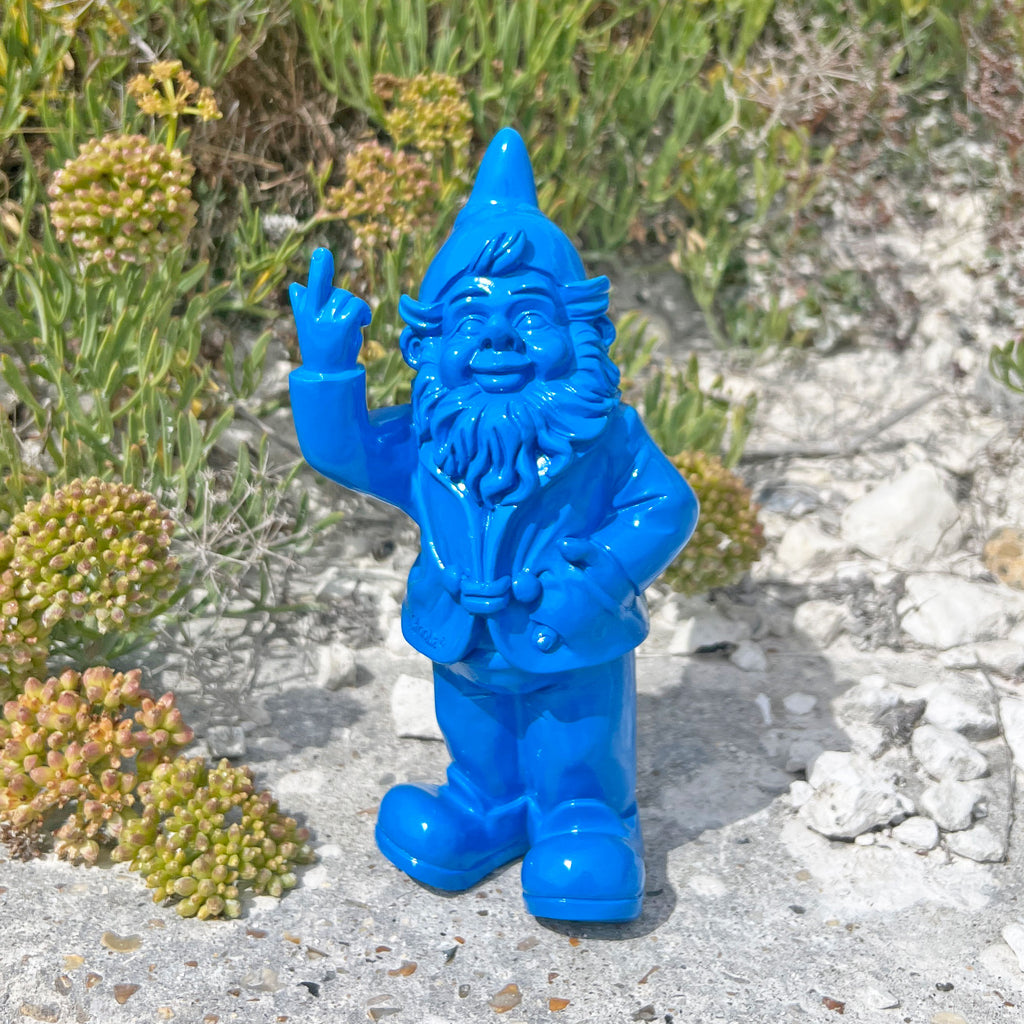 Blue garden gnome figurine standing on a rocky surface with greenery in the background